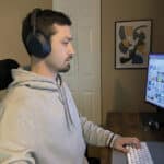 Person in a gray hoodie with large over-ear headphones sits at a desk, using keyboard and mouse as the monitor shows a grid of images.