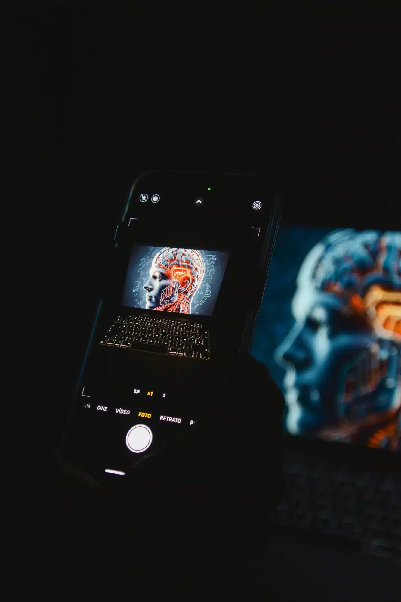 Dark scene with a smartphone showing a side profile of a head with an illuminated brain, while a blue-toned brain image glows on a nearby monitor.