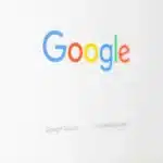 Google logo in multicolored letters on a white background with a faint search bar below.