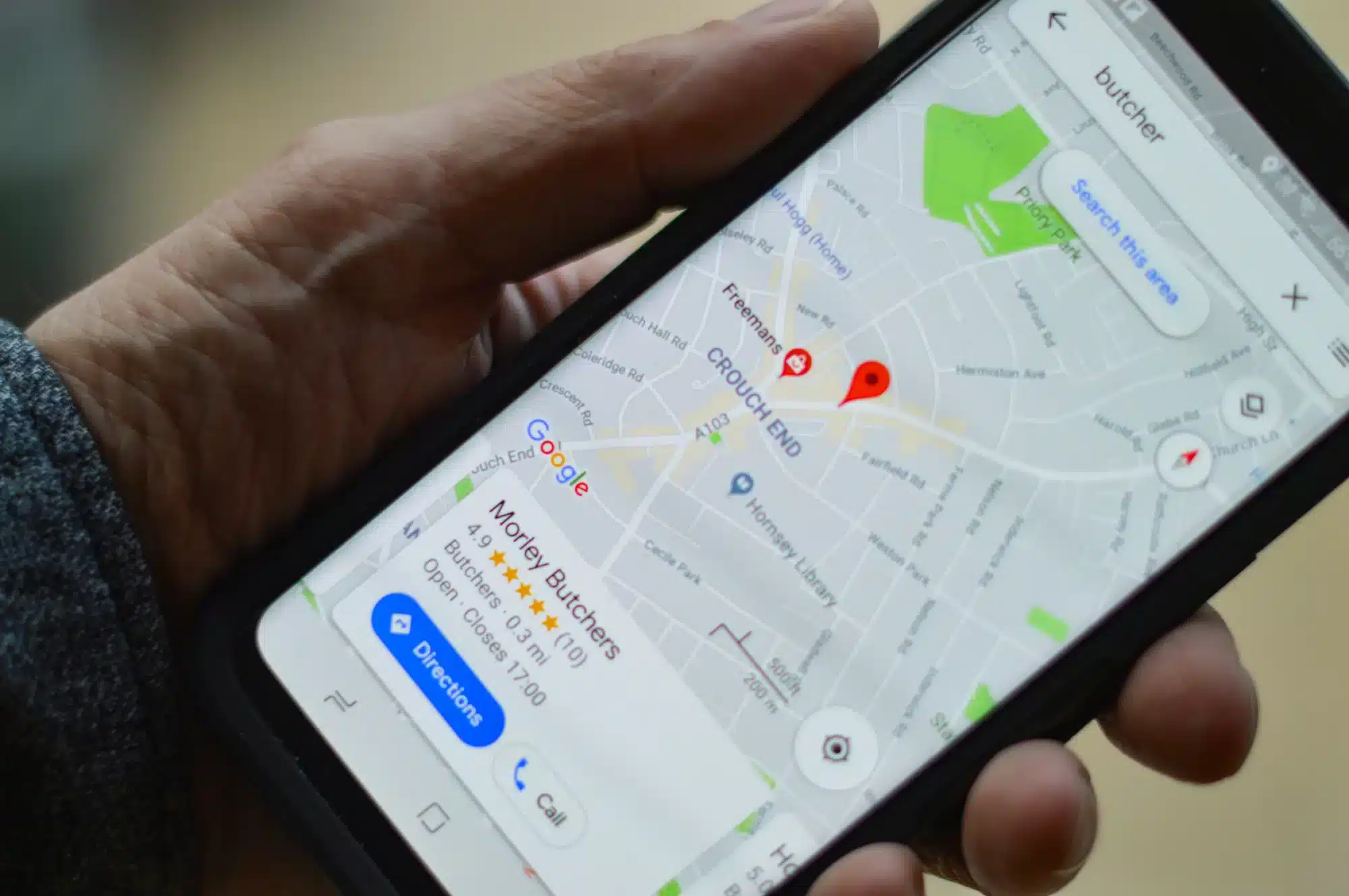 Hand holding a smartphone showing Google Maps with red location pins around a butcher shop.
