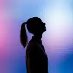 A silhouette of a person in profile with a ponytail against a vibrant pink-to-blue gradient background.
