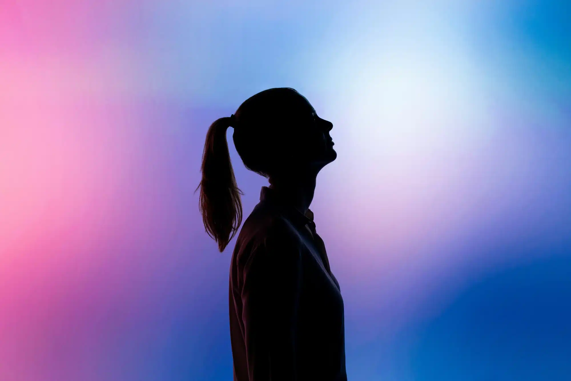 A silhouette of a person in profile with a ponytail against a vibrant pink-to-blue gradient background.