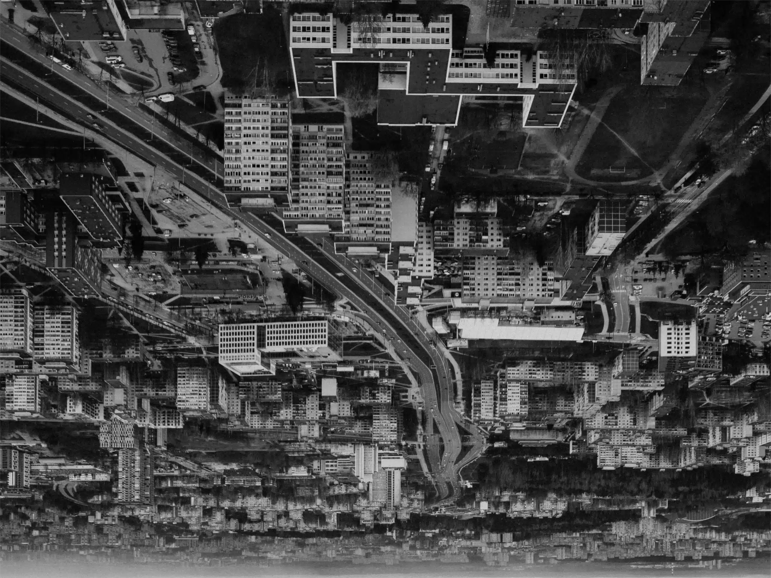 Aerial view of a dense city with many high-rise buildings and a curved elevated highway cutting through, in grayscale.