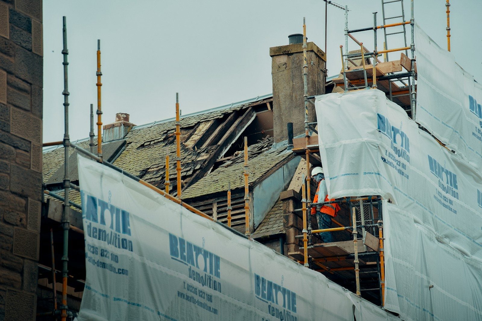 Building under renovation with scaffolding, protective sheeting, and a worker